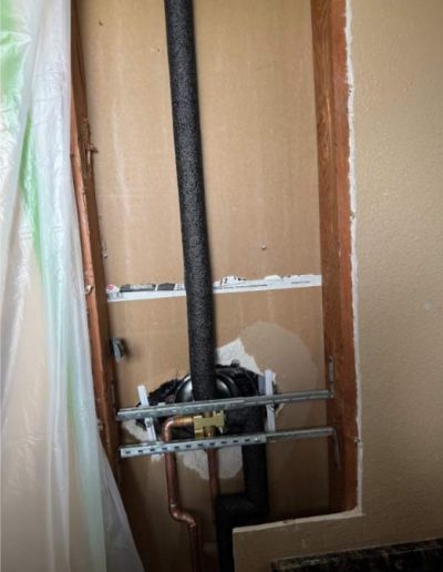 plumber installing a new shower valve, showing the valve body and its connections to water pipes within the bathroom wall.