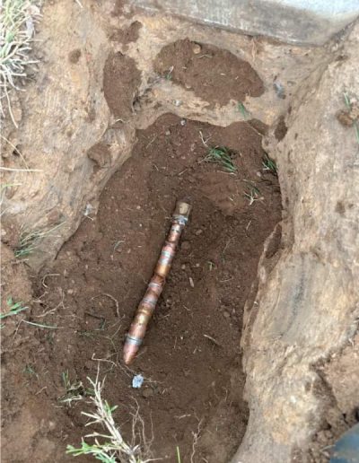 exposed copper and PVC water pipes in a trench, showing a repair or modification to residential water lines near a foundation