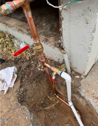 newly installed water pipes with a red-handled valve, illustrating a section of a water line replacement project in an outdoor setting